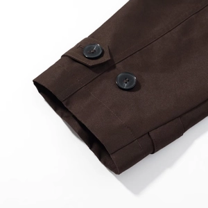 Close-up of deep brown trench coat cuff featuring black button and decorative strap detail