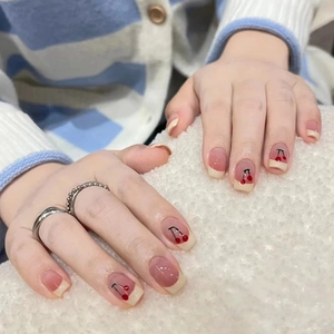 Detail of French tip press-on nails with red cherry designs and a soft pink gradient base
