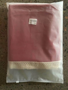 Folded red cotton tablecloth with white tassel lace border in plastic packaging