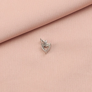 Detailed silver heart-shaped stainless steel pendant setting with four prongs on pink fabric
