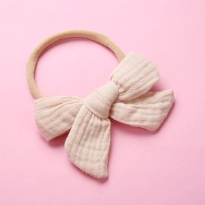 Detail of baby muslin headband with soft beige cotton bow on elastic nylon band