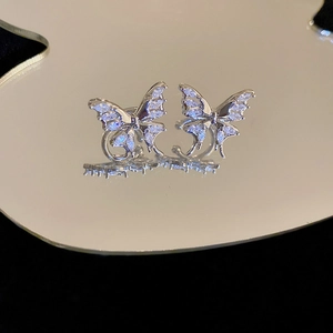 Macro shot of silver zircon butterfly ear clips reflecting on a sleek mirrored surface