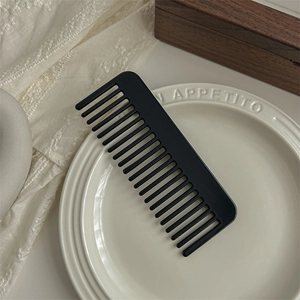 Close-up of black matte wide-tooth comb for hair styling on an elegant ceramic plate
