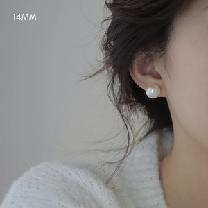 Detail shot of a 14mm elegant white pearl earring worn by a model in knitwear