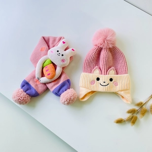 Close-up of knit hat and scarf set featuring 3D bunny decor and plush pom-poms