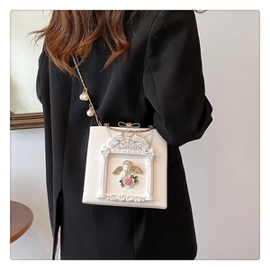 Detailed close-up of baroque angel relief and pearl chain on a white box handbag