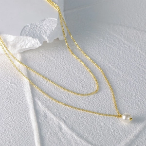 Detail of a double-layered gold chain necklace with a round white pearl pendant