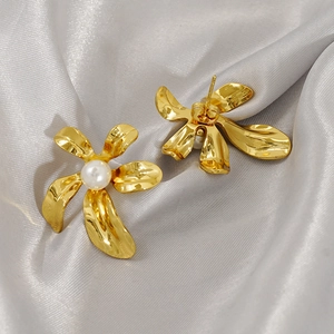 Elegant gold flower earrings with white pearl center on smooth silver silk fabric background