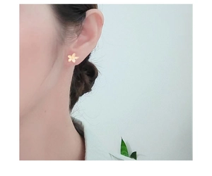 Close-up of a delicate gold flower stud earring worn on a model's ear for a stylish look