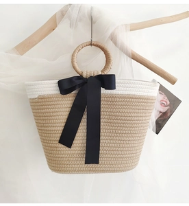 Detail of hand-woven tote bag featuring a round handle and a black ribbon bow decoration