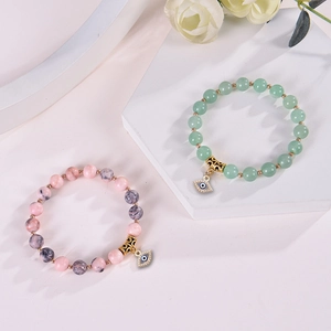 Pink Zebra Jasper and translucent green beaded bracelets with Evil Eye charms on stone display