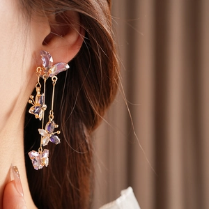 Détail de boucles d'oreilles dorées à pampilles avec papillons en cristal violet