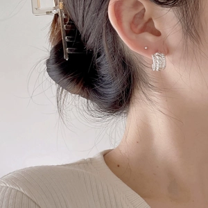 Detail of twisted silver hoop earrings showing metallic texture on model's ear