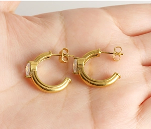 Détail de boucles d'oreilles dorées en C avec zircon unique sur un fond de main humaine