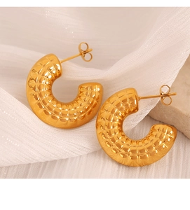 Detailed view of golden C-shaped hoop earrings with quilted pattern on white silk fabric