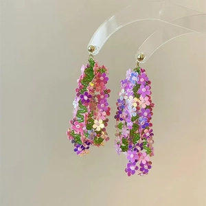Close-up of dangling floral earrings with colorful sequins and green beads on a clear stand