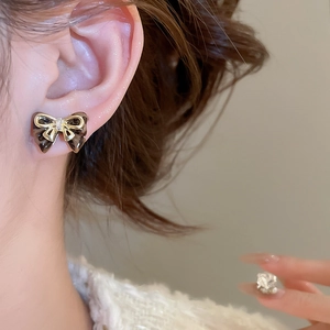 Close-up of model wearing brown and gold bow stud earrings with sparkling center zircon