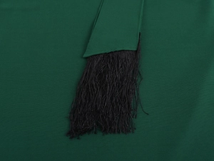 Dettaglio della trama del tessuto verde scuro e delle nappe nere dell'abito lungo