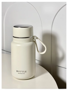 Close-up of cream white insulated water bottle with silicone carry handle and silver cap