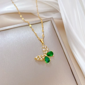Detailed macro view of a gold butterfly necklace with green gems and white zircons