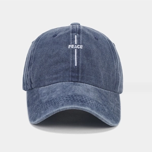 Gros plan détaillé de la broderie PEACE blanche sur une casquette en coton lavé bleu foncé