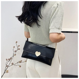 Close-up of black glossy leather envelope bag with gold heart clasp on a female model