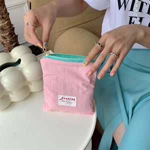 Close-up of pink and mint green mini storage pouch with a zipper being opened by a hand