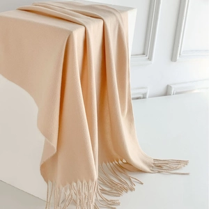 Elegant cream beige cashmere style scarf with tassels draped on a white minimalist cube