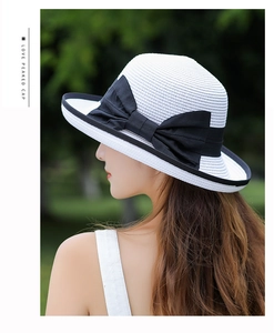 Detail of white straw sun hat featuring a black brim and large ribbon bow decoration