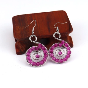 Detail of handmade wire wrapped earrings with purple beads on a rustic wooden stand