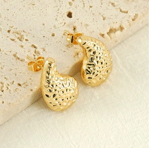 Détail macro de boucles d'oreilles goutte d'or avec texture martelée sur travertin
