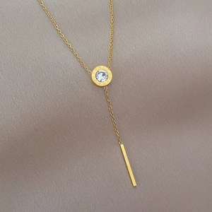 Macro shot of gold tassel necklace with Roman numeral engraved ring and zircon pendant