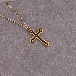 Detailed view of a gold cross pendant with black enamel inlay on a textured gray background