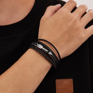 Detail view of men's layered leather bracelet featuring a silver metal arrow charm on wrist