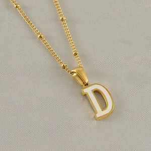 Detail of a golden D-letter pendant with white enamel inlay and elegant bead chain
