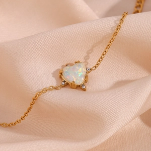 Detailed shot of a gold heart bracelet with opal and diamonds on soft beige silk