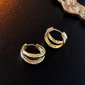 Detail of layered gold metal C-shaped hoop earrings on black leather surface