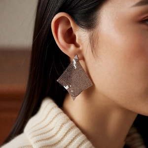Vue rapprochée de boucles d'oreilles dorées avec un tissage métallique en forme de losange