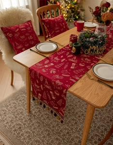 Detail view of red Christmas table runner featuring gold foil patterns and fringe tassels