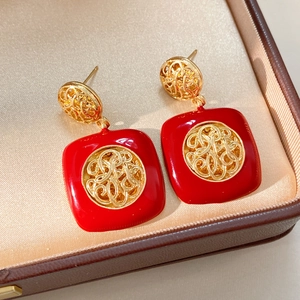 Primo piano di orecchini pendenti quadrati in smalto rosso stile vintage con dettagli in oro.