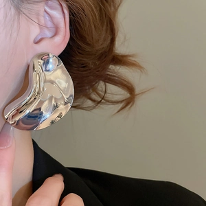 Close-up of polished silver irregular wave earring worn by a model on warm background