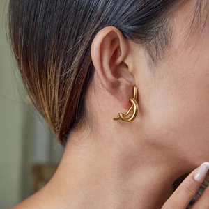 Close-up of a model wearing minimalist golden hoop earrings with a sleek curved design