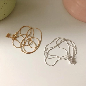 Detailed view of silver and gold link chains on a minimalist beige background