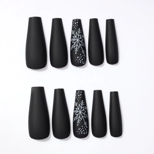 Detail view of long coffin press-on nails in matte black with white snowflake patterns