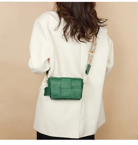 Detail of green woven leather shoulder bag with a patterned wide strap on model