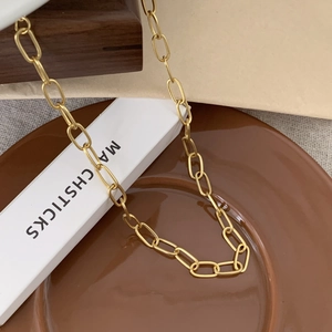 Detailed close-up of golden paperclip chain necklace on a ceramic plate display