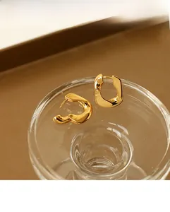 Macro shot of gold-plated wavy earrings on a glass edge with a polished mirror finish