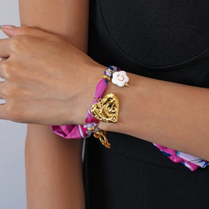 Detail of pink fabric bracelet with golden heart pendant and white smiley face charm