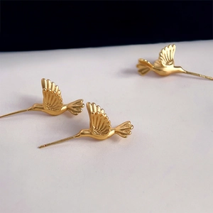 Macro detail of golden matte hummingbird earrings with artistic feather carvings