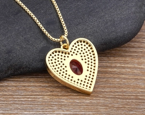 Macro detail of gold plated heart pendant back with red gemstone and hollow-out design
